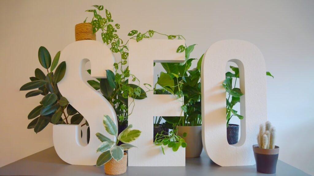 Logo de SEO físico con plantas atrás adornándolo, ejemplificando el cambio de imagen de un material reutilizado.
